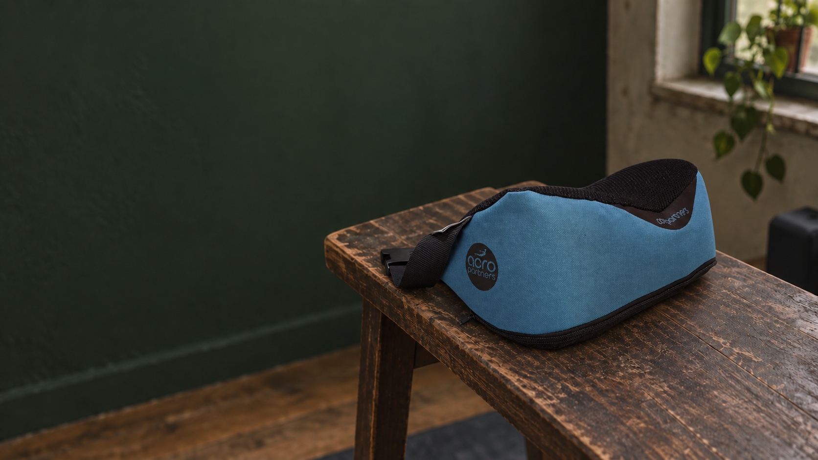 Blue AcroPartners support pillow on a wooden table, showing its shape, fabric and straps.