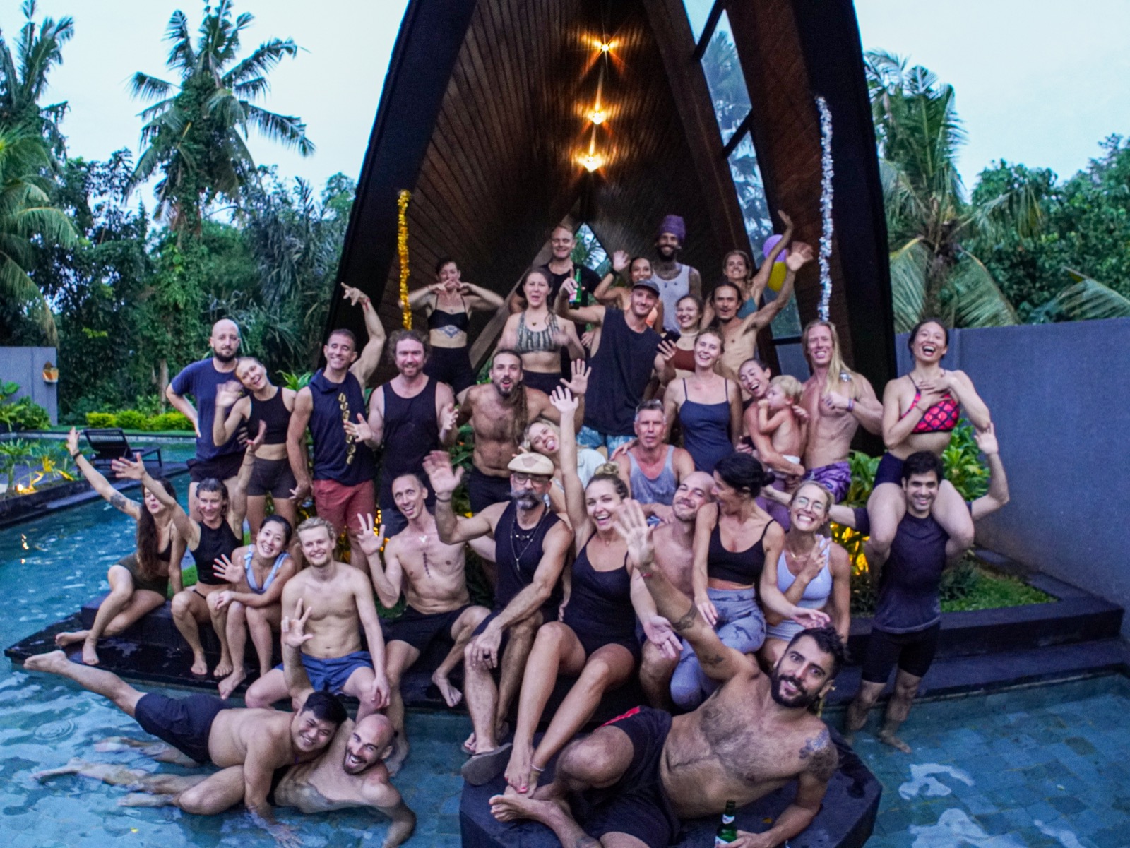 An Acro Villa group smiling and waving together beside a pool surrounded by tropical greenery